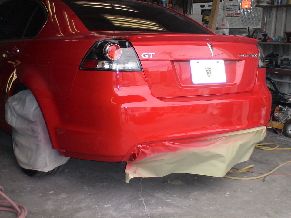Red sedan's rear bumper is taped off for painting. GT badge visible on trunk