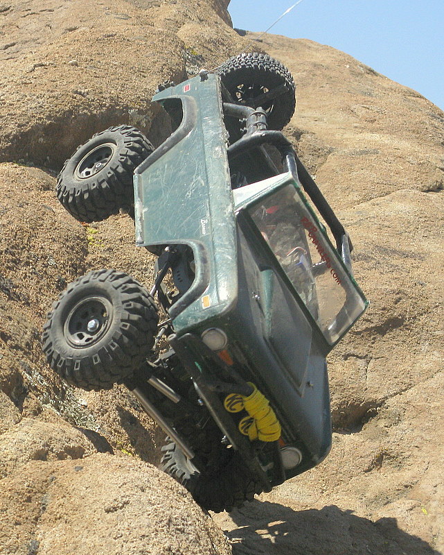 Green rock crawler vehicle tipped over on a rocky incline