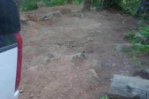 1993 Ford Bronco - The rear corner of a white SUV is visible on a rough, rocky dirt path through a wooded area.