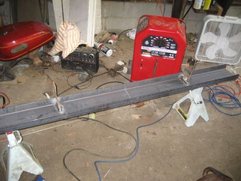 1995 Ford Bronco - A red welder and a metal beam are set up in a garage, with a motorcycle gas tank and a boombox nearby.