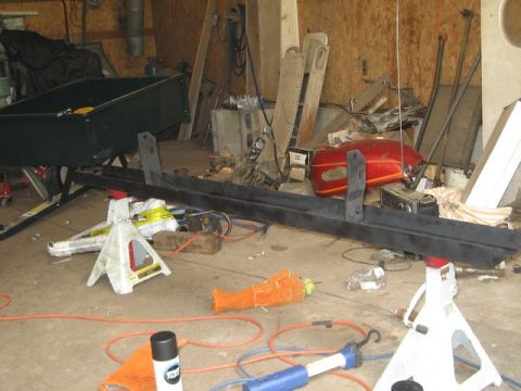 1995 Ford Bronco - A metal automotive part is supported by jack stands in a cluttered garage setting.