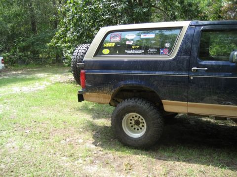 1995 Ford Bronco - This Ford Bronco, seen from the side, is covered in mud and has numerous stickers on its rear window.