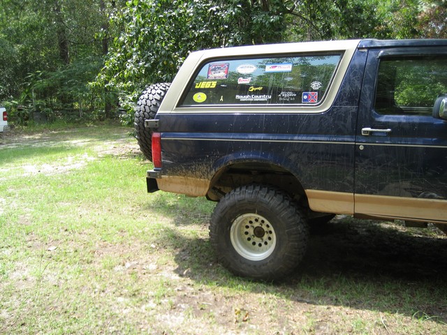 Dark blue Ford Bronco with tan trim, spare tire on rear, covered in mud and stickers on rear window