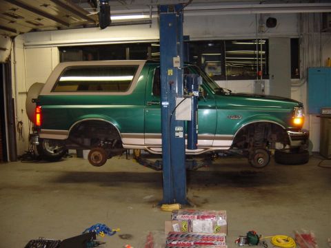1996 Ford Bronco - A green 1996 Ford Bronco is raised on a car lift in a garage, undergoing service.