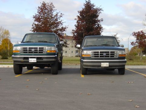 1996 Ford Bronco - Two Ford trucks, likely from the mid-1990s, are parked in an outdoor lot under a cloudy sky.