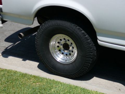 1988 Ford Bronco - Close-up of a vehicle's rear tire and exhaust pipe, parked on a sunny day.