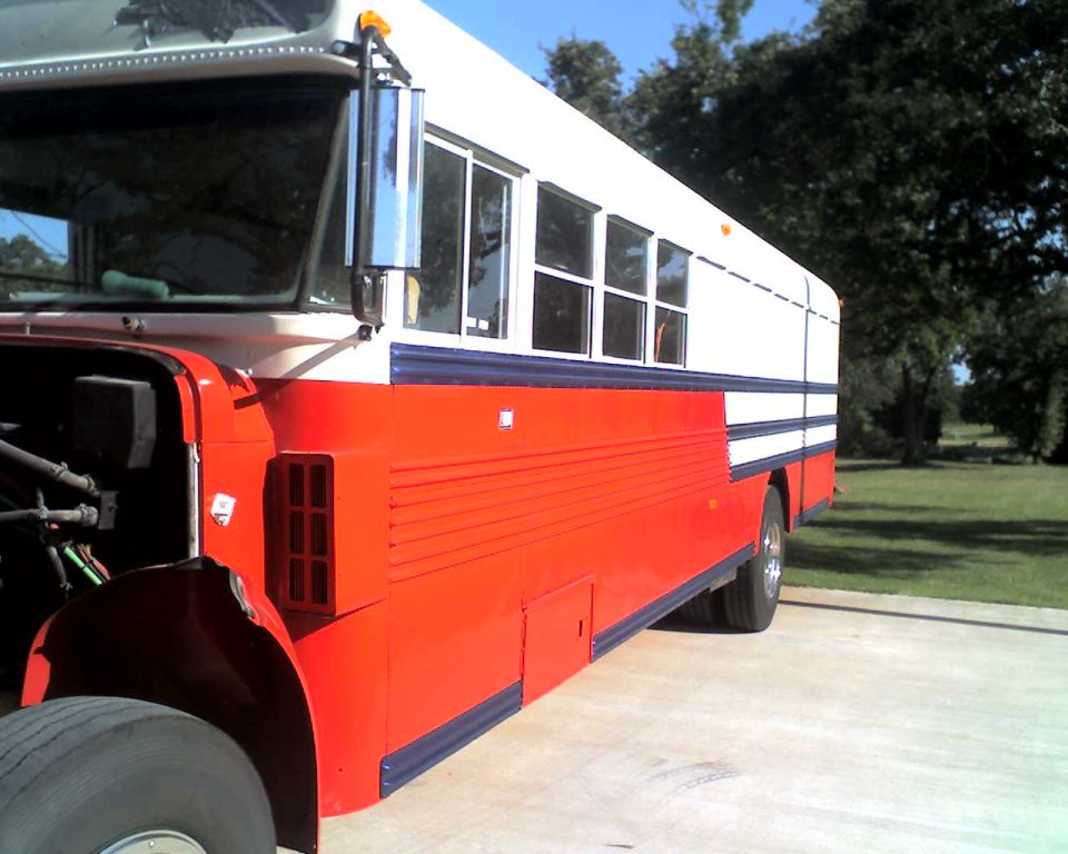 Side view of a red and white school bus with its front fender removed