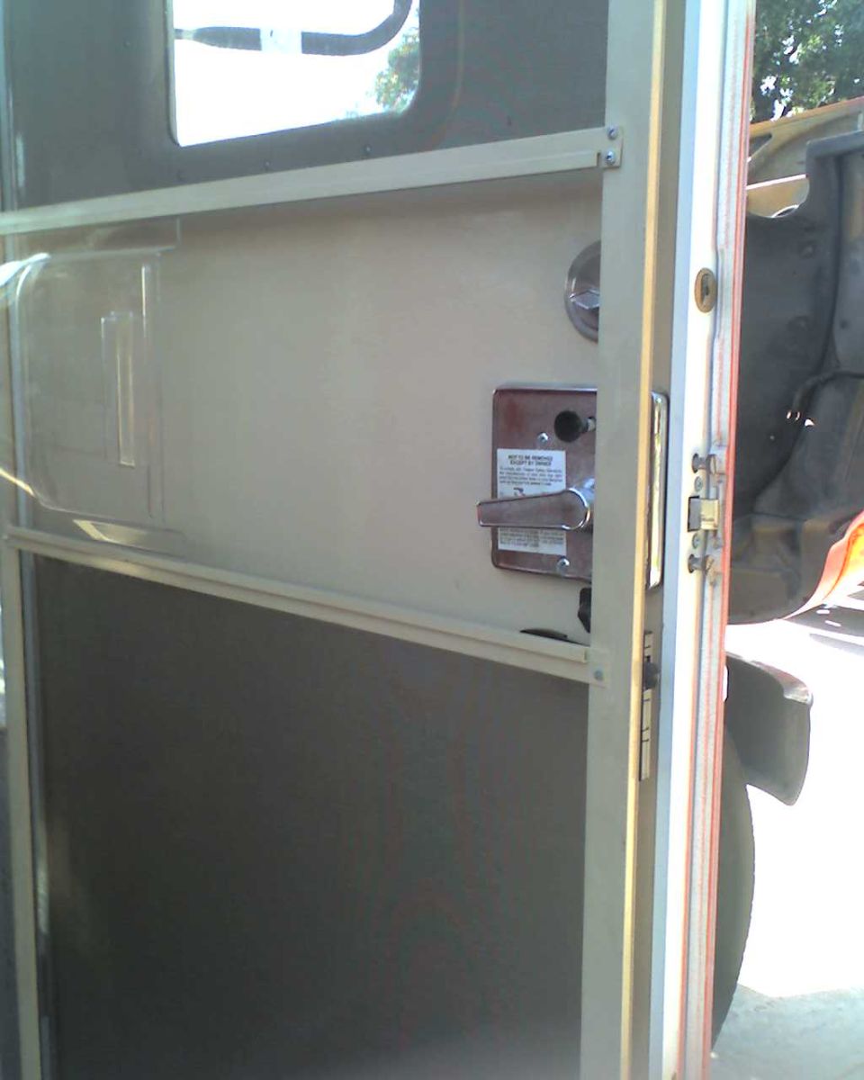 Interior view of a school bus door, showing the latch mechanism and a small compartment
