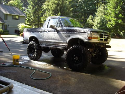 1993 Ford Bronco - A lifted 1993 Ford Bronco is being washed in a driveway with a hose and bucket.