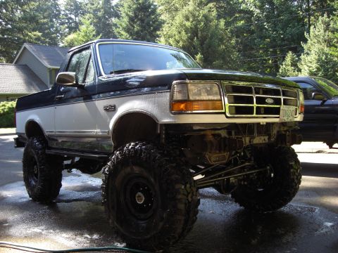 1993 Ford Bronco - This lifted Ford truck features a two-tone paint scheme and is parked outside on a wet driveway.