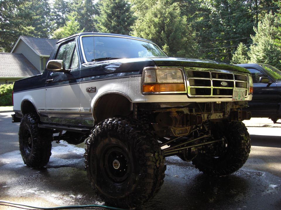 Lifted Ford truck with large tires, two-tone paint, and aftermarket bumper