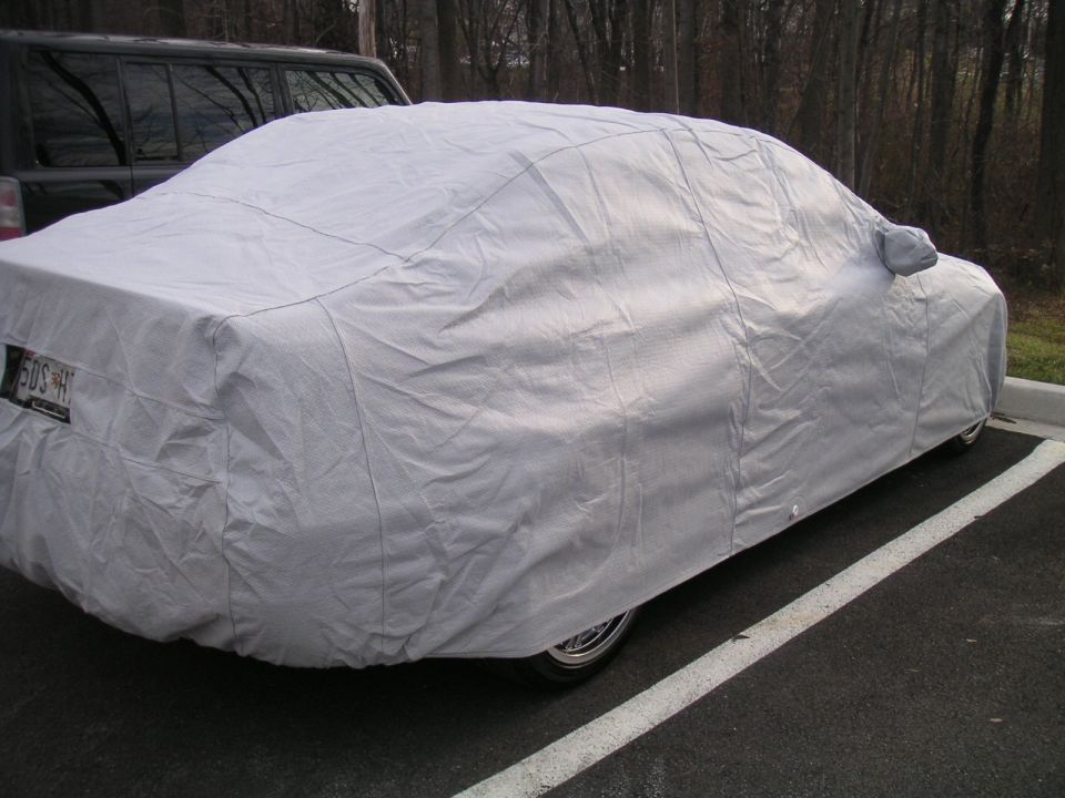 Car covered with a grey cover parked next to a dark SUV