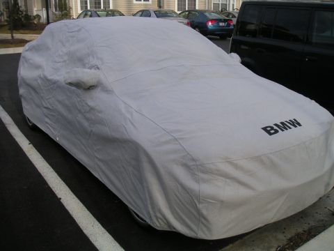 2002 BMW M3 - A car is completely covered by a gray car cover with the BMW logo visible on the hood.