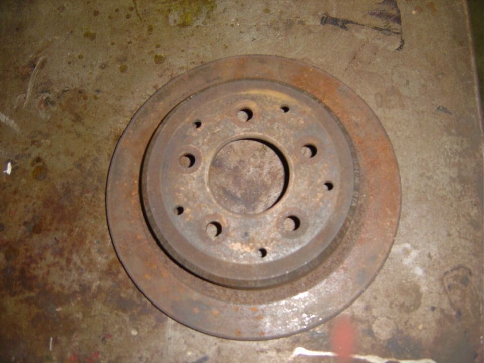 Rusty brake rotor with multiple bolt holes on a concrete surface