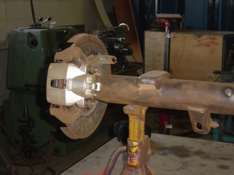 1996 Ford Bronco - A rear axle assembly with a disc brake system is shown, supported by a jack stand in a workshop setting.