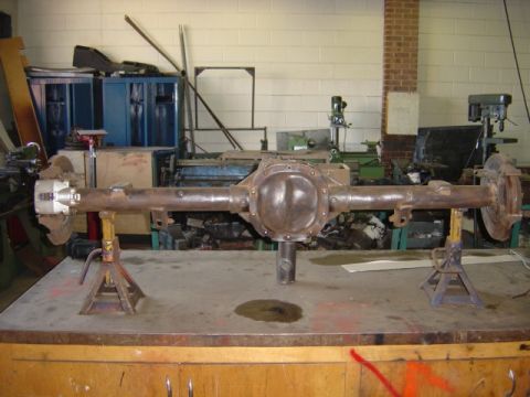 1996 Ford Bronco - A rusty rear axle assembly is displayed on jack stands in a workshop environment.