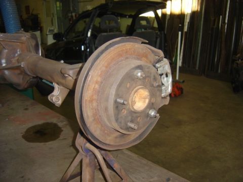 1996 Ford Bronco - Close-up of a vehicle's rear axle and brake system, with a car in the background.