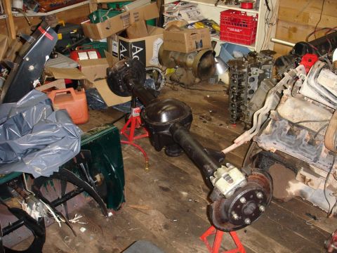1996 Ford Bronco - A disassembled rear axle assembly with disc brakes is shown in a garage setting, surrounded by various car parts and storage items.