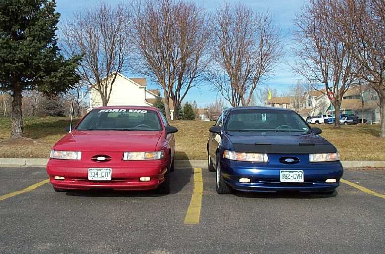 Two Ford Taurus sedans, one red and one blue, parked front-end to front-end in a lot