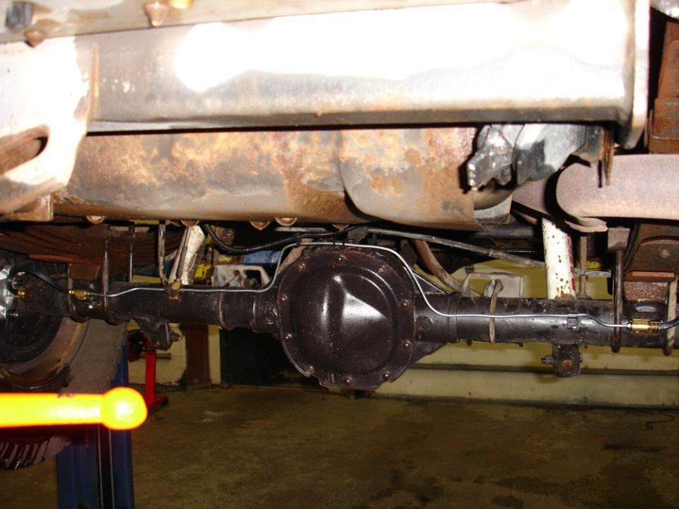 Underside view of a vehicle's rear axle and differential assembly. Shows brake lines and suspension components