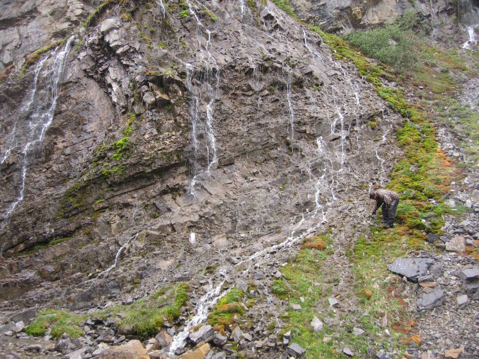 Person kneeling on a mossy, rocky slope with waterfalls.