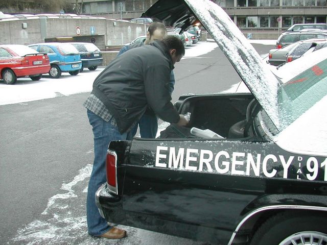 Man working under the open trunk of an Emergency 911 police car