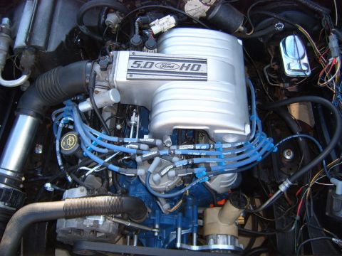 1973 Ford Ranchero - A close-up view of a Ford 5.0 HO engine, featuring a silver intake manifold with blue spark plug wires and a black air intake tube.