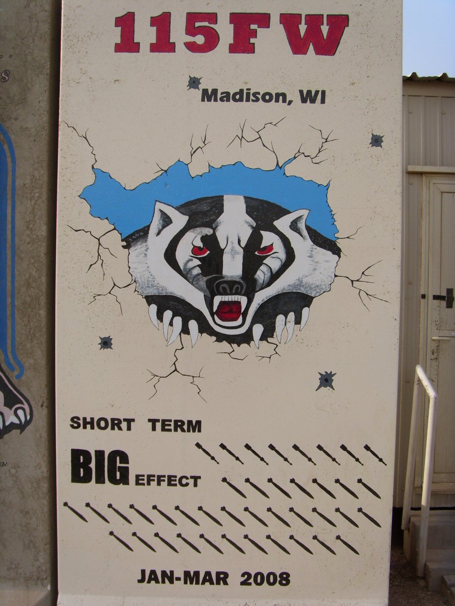Mural of a badger breaking through a wall, with text '115FW Madison, WI' and 'SHORT TERM BIG EFFECT' and rows of bombs