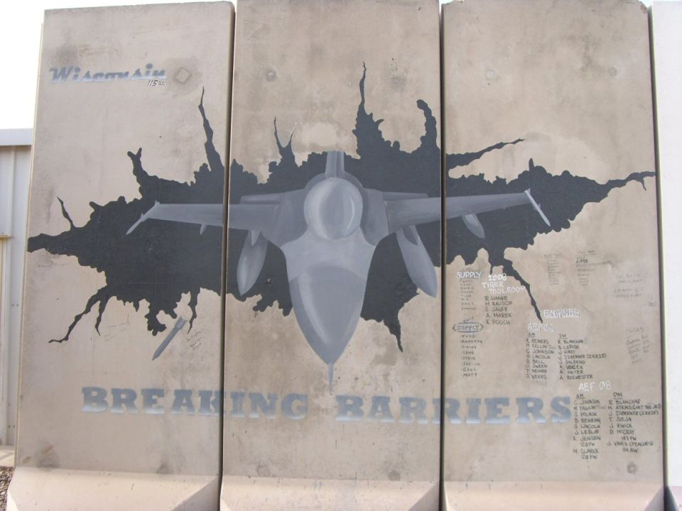 Mural on concrete barriers depicting a jet breaking through a wall, with text 'BREAKING BARRIERS' and lists of names