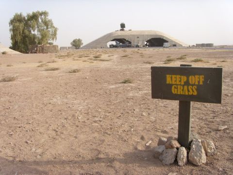1978 Ford Bronco - A joke wooden sign reading "KEEP OFF GRASS" in yellow stencil letters, propped up with rocks in bare desert dirt. In the background sits a…