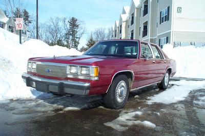 1991 Ford Crown Victoria LTD - A red sedan sits parked in a snowy lot next to an apartment complex.