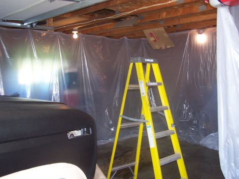 1986 Ford Bronco - A black Ford Bronco's front is visible, partially painted, with a yellow ladder and plastic sheeting in a garage.