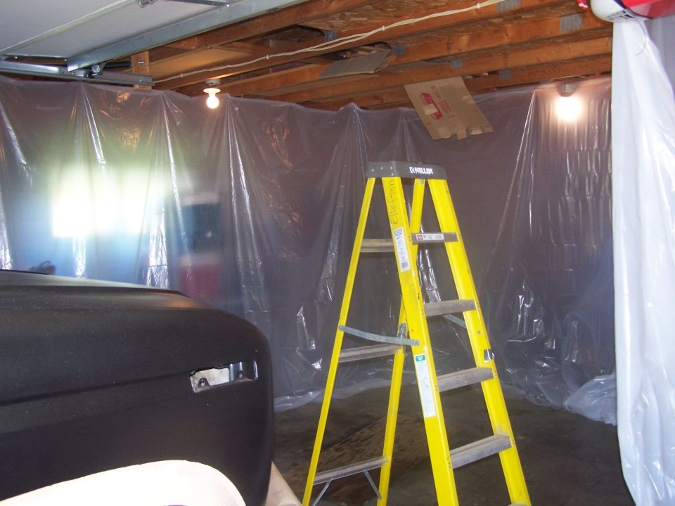 Black Ford Bronco front fender and headlight area, partially painted, with a yellow ladder and plastic sheeting in the background