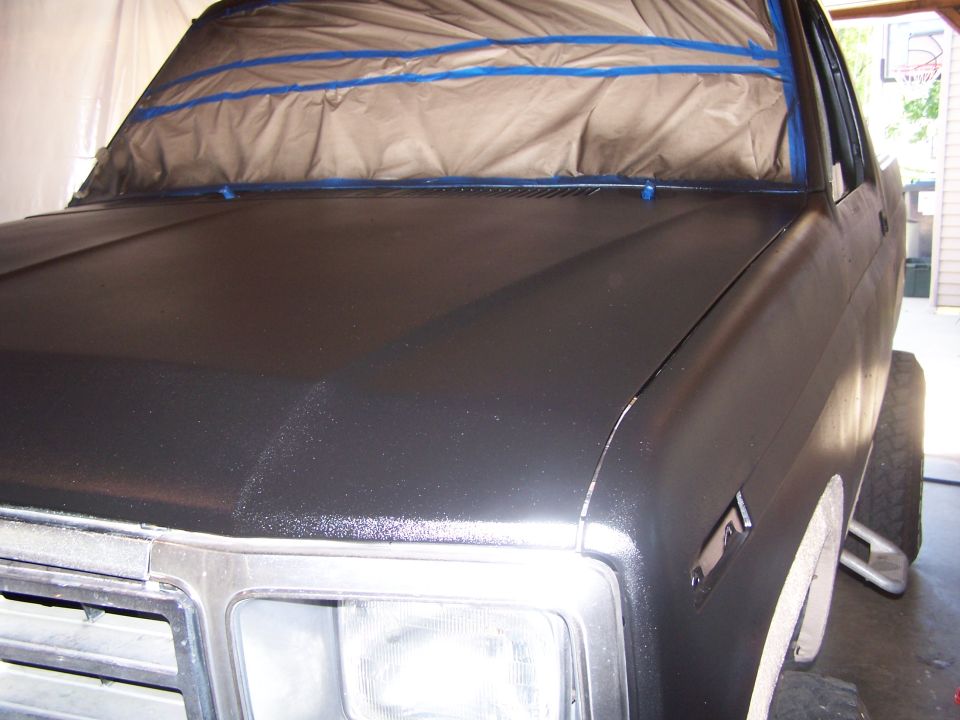 Hood and fender of a truck covered in masking tape and plastic, ready for paint. Headlight and grille visible