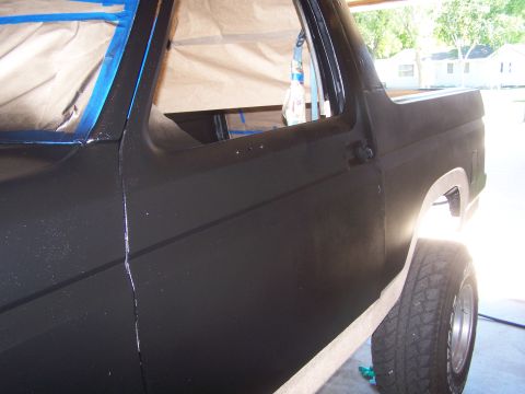 1986 Ford Bronco - A black Ford Bronco is partially masked and prepped for painting, showing its side profile.
