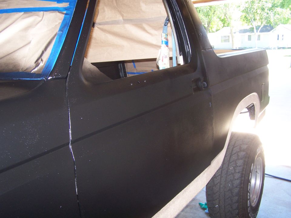 Black Ford Bronco side view, undergoing paint preparation with masking tape