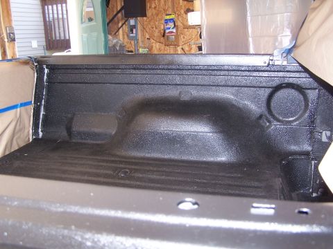 1986 Ford Bronco - The bed of a truck is shown with a fresh black textured liner and protective tape applied to the edges.