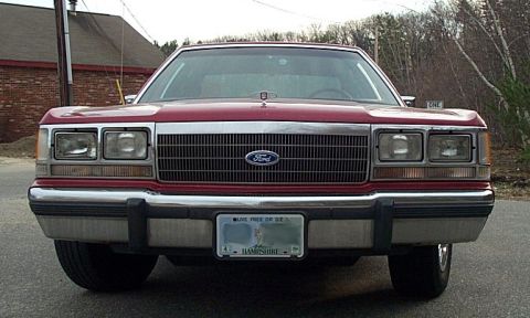 1991 Ford LTD Crown Victoria - Head-on front view of a burgundy Ford LTD Crown Victoria showing the wide chrome-framed grille with Ford blue oval, quad rectangular headla…