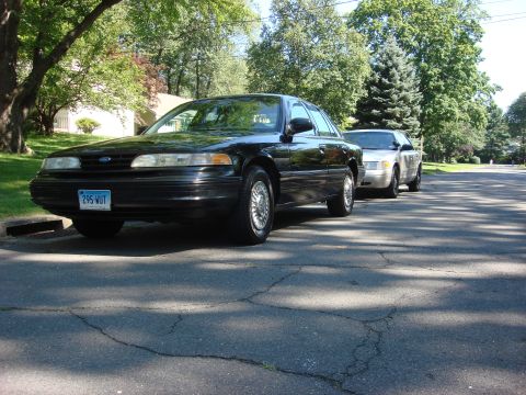 2003 Ford Crown Victoria - Two Ford Crown Victorias are parked on a residential street on a sunny day.