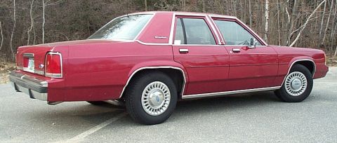 1991 Ford LTD Crown Victoria - Rear three-quarter passenger-side view of a burgundy/red Ford LTD Crown Victoria four-door sedan parked on asphalt in front of bare winter…