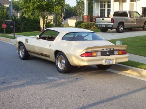 1979 Chevrolet Camaro - A tan 1979 Chevrolet Camaro Z28 is parked on the street in front of a house, with a silver pickup truck in the driveway.