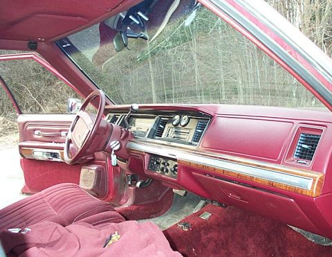 1991 Ford LTD Crown Victoria - Wide interior view across the burgundy dash of a boxy Ford full-size sedan, showing the woodgrain dash appliqué, center vents and rotary cl…