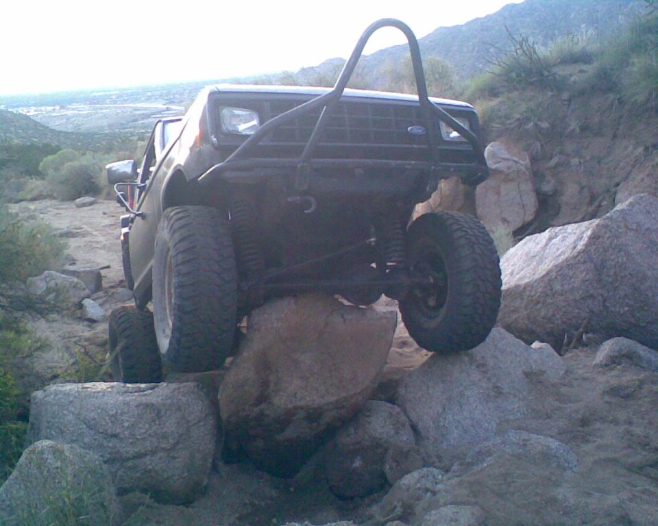 Dark lifted Ford SUV flexing over boulders on a rocky desert trail, front view