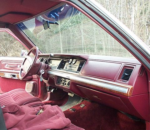 1991 Ford LTD Crown Victoria - Passenger-side view across the red interior of a boxy Ford full-size sedan, showing the burgundy dash and door panels, woodgrain trim strip…