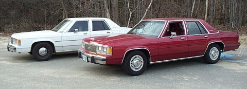 1991 Ford LTD Crown Victoria - Two sedans, a red 1991 Ford Crown Victoria LTD and a white sedan, are parked outdoors.