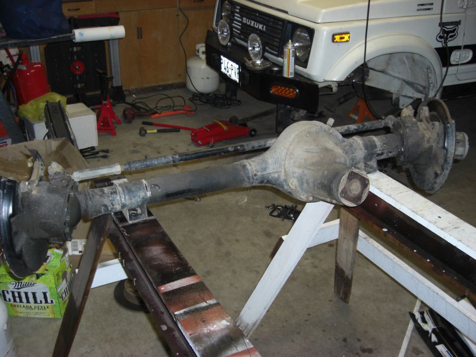 Removed axle assembly on sawhorses in garage with white Suzuki Samurai behind