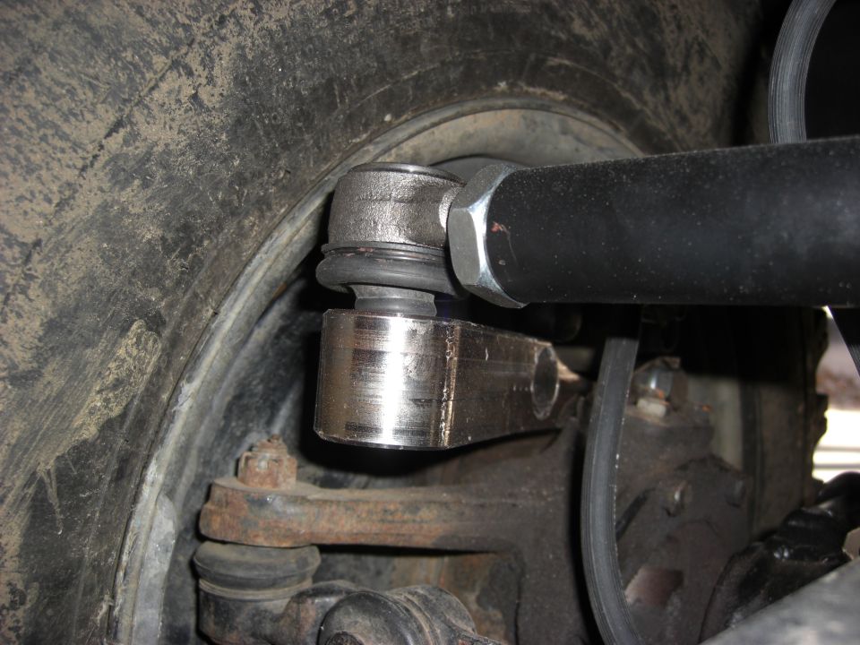 Rod-end tie rod bolted to steering arm over the knuckle behind a muddy tire