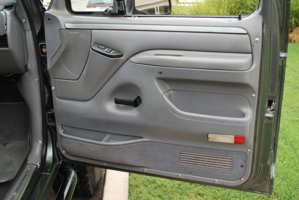 Gray interior door panel with manual window crank, power lock button, and storage compartments