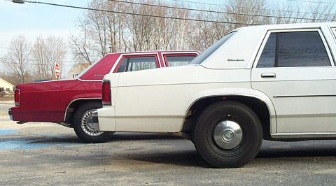 1991 Ford LTD Crown Victoria - Two sedans are parked side-by-side, showing their rear sections and wheels.