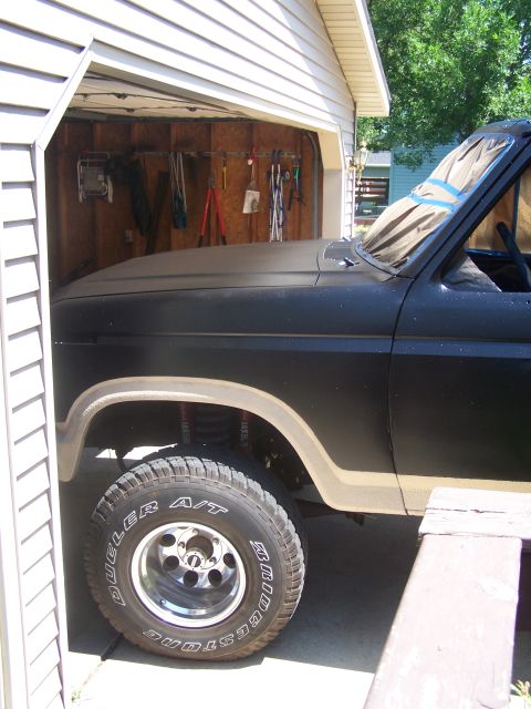 1986 Ford Bronco - A black Ford Bronco with tan trim and off-road tires is partially visible inside a garage.
